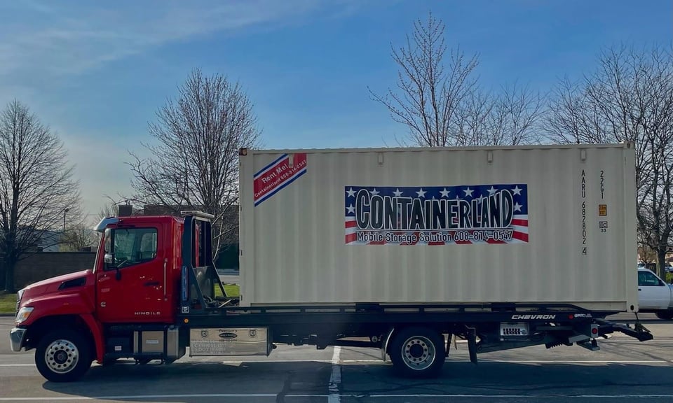 Flatbed tow truck with shipping container on it for delivery.